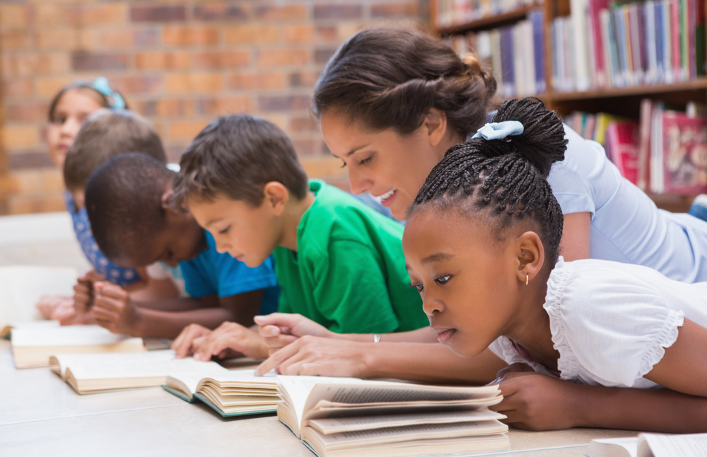 Cute pupils and teacher lying on floor in library at the elementary school-2